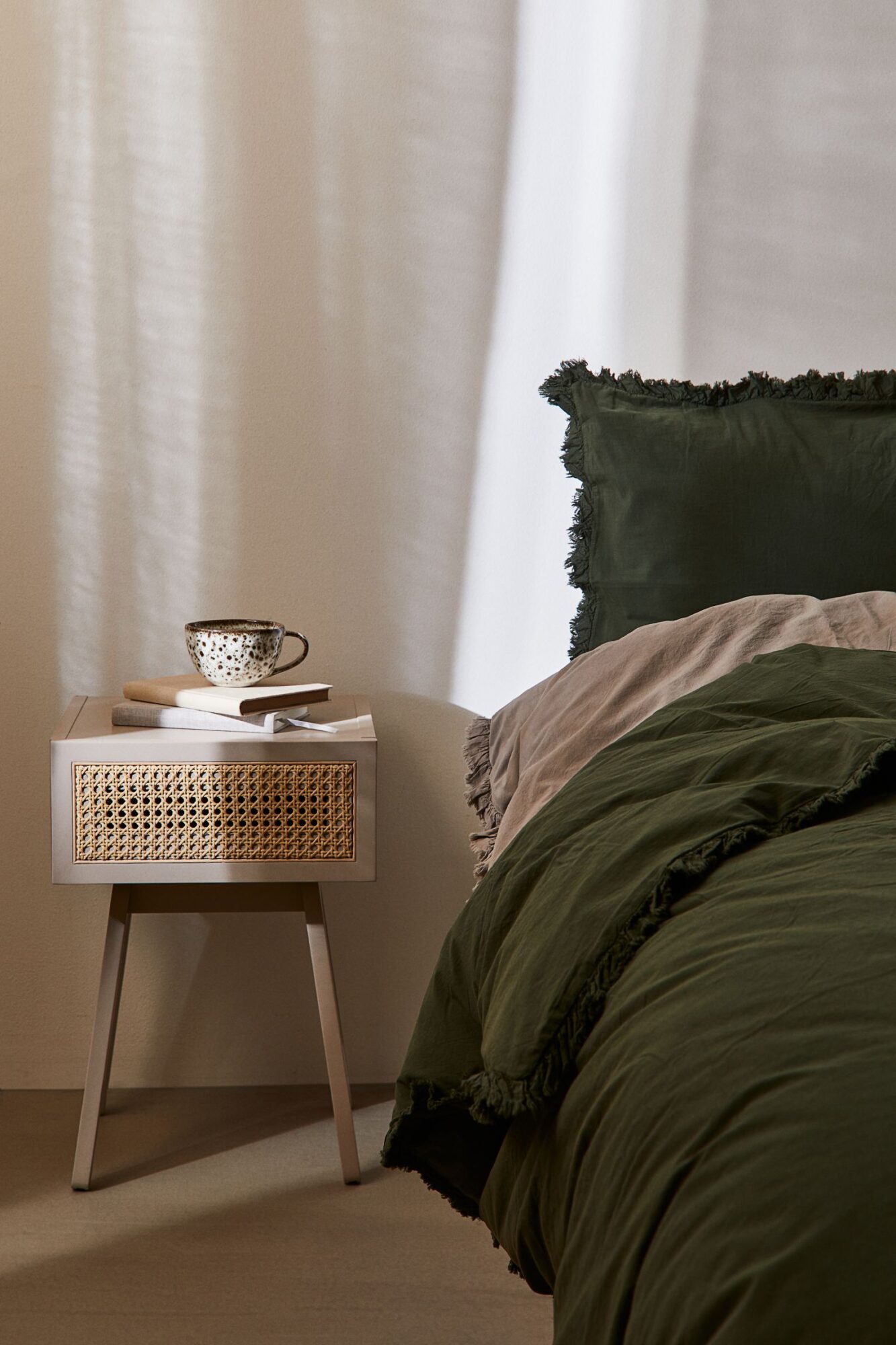 Boho-Style Nachttisch aus Rattan und hellbeigen Holz in moderner Optik mit Rattanschublade und vier Holzbeinen in einem gemütlichen Schlafzimmer von H&M